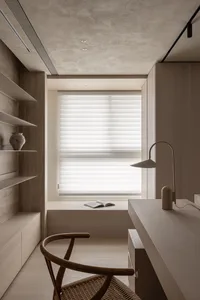 A minimalist office space featuring a wooden chair, concrete walls, and a sleek desk lamp.