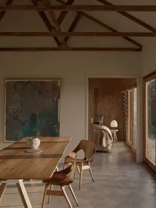 A minimalist residential space featuring wood furniture and a concrete floor, with a bedroom in the background.