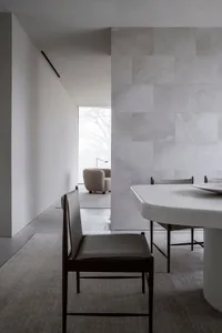 A minimalist dining room with white marble walls and a white marble dining table.