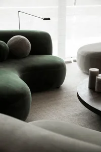 A modern living room featuring a green velvet sofa with a unique, organic shape, accompanied by a round table and large floor