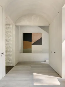 A minimalist interior design featuring a modern concrete wall with geometric art, white walls, and gray flooring.