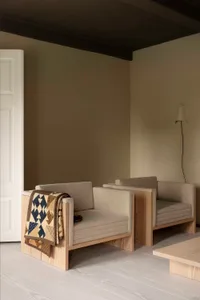 A modern interior featuring wooden furniture with a quilt draped over one of the chairs.