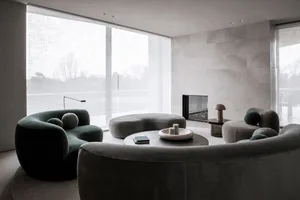 Modern living room with comfortable velvet sofas and matching ottomans, round coffee table, and a sleek fireplace.