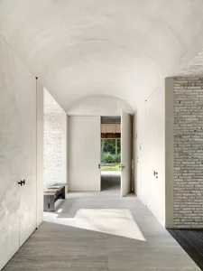 A minimalist hallway with concrete walls, wooden doors, and a large window at the end.