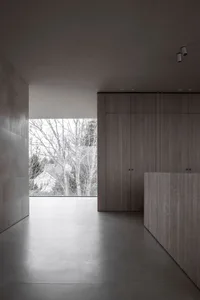 Modern minimalist interior space with wooden elements and concrete floor, featuring a large window showing a view of a tree-l