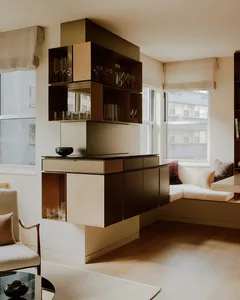 A modern minimalist living room with a neutral color palette, featuring a floating storage unit and a corner window seat.