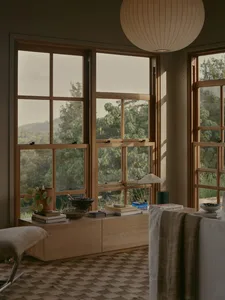 A cozy, minimalist living room with wooden furniture and large windows overlooking nature.