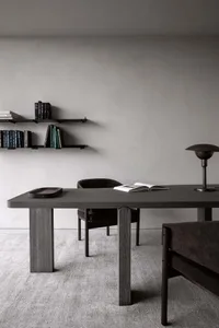A modern minimalist office space featuring a dark wooden table and a bookshelf filled with books and other items on a gray ca