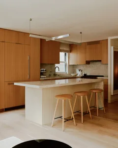 Modern kitchen interior with wood cabinets, marble countertops, and a central island with stools.