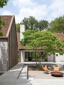 A modern residential exterior with brick and concrete materials and a spacious courtyard with a tree and seating area.