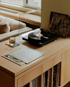 A wooden furniture piece with a record player, records, and a glass of liquid on top.