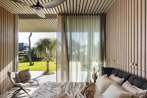 A minimalist bedroom with wooden walls, a bed, and a curtain lets in natural light.