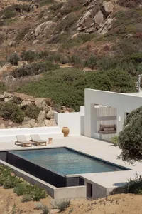 Modern minimalist residential patio featuring a concrete pool and sun loungers against a natural hillside backdrop.