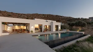 A minimalist villa with a concrete exterior, featuring a modern pool and large windows overlooking the landscape.
