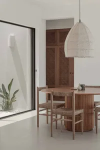 Modern dining room featuring a wooden table with straw-wrapped chairs, natural light from a window with a textured interior w