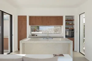 A modern kitchen featuring a large central island made of concrete with a sink and a window overlooking a stone wall.