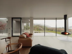 A modern living room with a glass wall overlooking a natural scene.