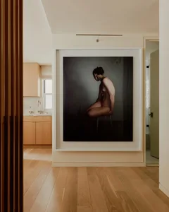 A minimalist interior photograph featuring a female model seated on a stool.