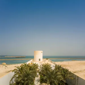A modern, cylindrical clay tower amidst tropical palm trees by the waterfront.