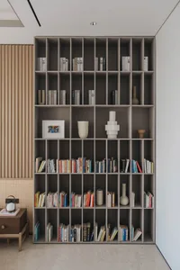 A minimalist bookshelf made of wood, filled with books and decorative vases.