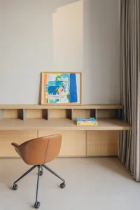 Minimalist home office with wooden furniture, a brown leather rolling chair, and a colorful abstract painting on the desk.