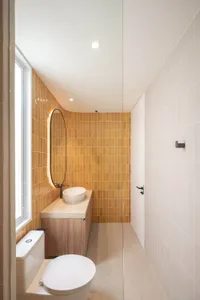 Modern bathroom featuring orange and cream square tiles, a white sink, and white toilet with a wooden vanity.