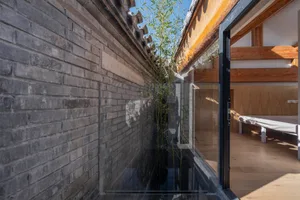 A modern bedroom with a wooden interior, featuring a bed with white sheets, wooden floor, and glass wall with bamboo plants.