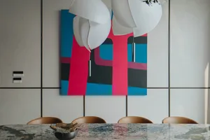 A modern dining room features a large, vibrant abstract painting as the centerpiece, accompanied by sleek, contemporary chair