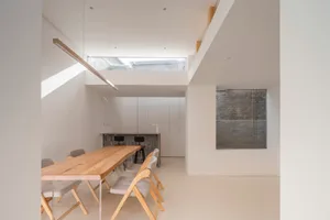 Modern kitchen and dining area with wooden table and chairs, light-colored walls, and floor-to-ceiling windows.