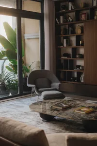 A modern living room featuring a round coffee table with a natural stone top, a gray upholstered chair, and a bookshelf fille
