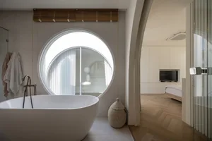 A modern bathroom with a freestanding tub, a round window, and a white marble finish.