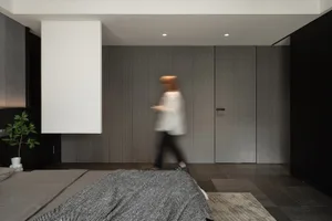 A minimalist bedroom featuring dark tones, a textured wall, and a bed with a patterned blanket.