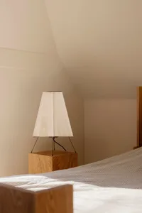 A minimalist bedroom featuring a wooden base lamp with a simple white fabric shade, creating a cozy and contemporary atmosphe
