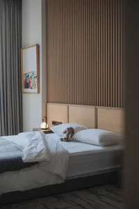 A minimalist bedroom featuring a white wooden headboard, white bedding, and a rabbit plush toy on the bed.