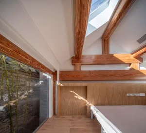 A modern minimalist bedroom featuring wooden beams and a skylight.