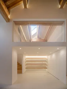 A minimalist space with white walls and wood elements, featuring a staircase illuminated by LED lighting from above.
