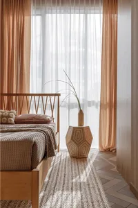 Minimalist bedroom with light-colored wooden frame, fabric bedding, and glass vase