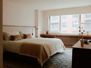 A minimalist bedroom with a textured patterned wall, a large window, and a wood-finished furniture set.