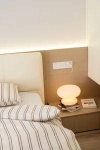 A minimalist bedroom with a white bed, striped bedding, and a wooden headboard and bedside table.