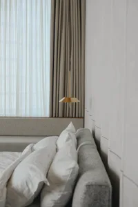 A minimalist grey bedroom with textile curtains and a fabric headboard.