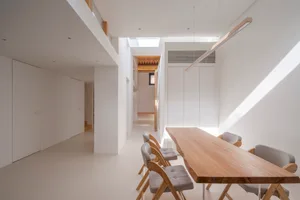 Modern, minimalist dining area with white walls, wooden table, and grey chairs.