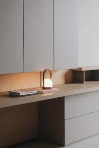 A minimalist interior design space featuring a wooden counter with books, a light lamp, and organized shelves.