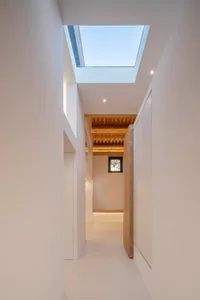 A narrow hallway with white walls and a wooden ceiling, featuring a skylight.