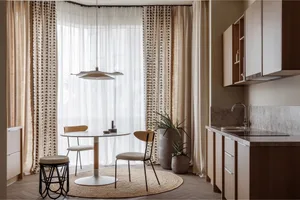 A modern kitchen with neutral tones, featuring a round table, chairs, and a potted plant under a pendant light.