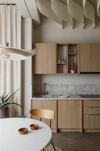 A modern kitchen with wooden countertops and cabinets, featuring a round table, bowls, and potted plant.