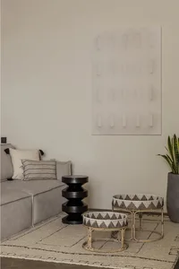 Modern interior design featuring a gray couch, black acrylic artwork, black and white patterned bamboo side tables, and a woo