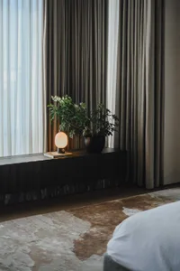Modern minimalist bedroom featuring fabric curtains, a reading lamp, and a plant on a floating nightstand.