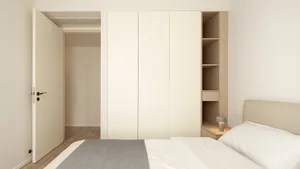 Modern minimalist bedroom with white furniture and fabric coverings.