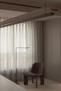 A minimalist bedroom with a brown upholstered chair, a black floor lamp, and white curtains.