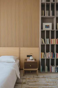 A modern minimalist bedroom featuring a bed with a wooden headboard, a wooden nightstand, and a large bookshelf filled with b